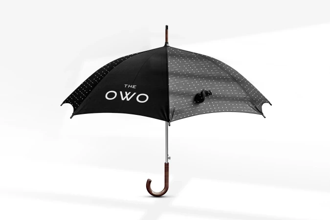 Open black umbrella with white polka dots and dark wood handle stands on a white background, displaying 'THE OWO' logo.