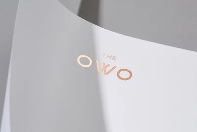 Copper foil embossed The Owo logo on white textured paper stationery against grey background
