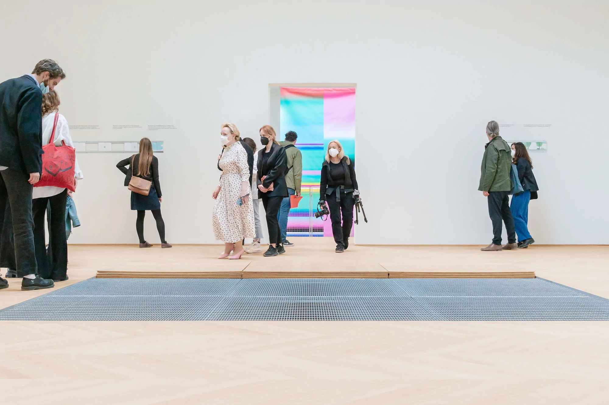 Visitors observe a contemporary art installation inside a modern art gallery, wearing face masks, in a wide indoor shot.