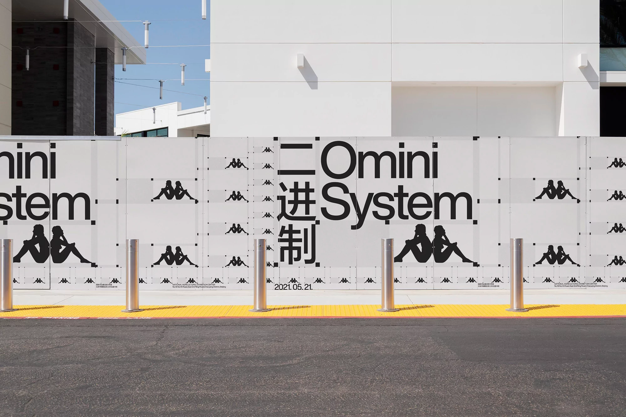 Outdoor urban scene with a Kappa-branded barricade featuring the Omini System logo and yellow pavement, captured on a sunny day.