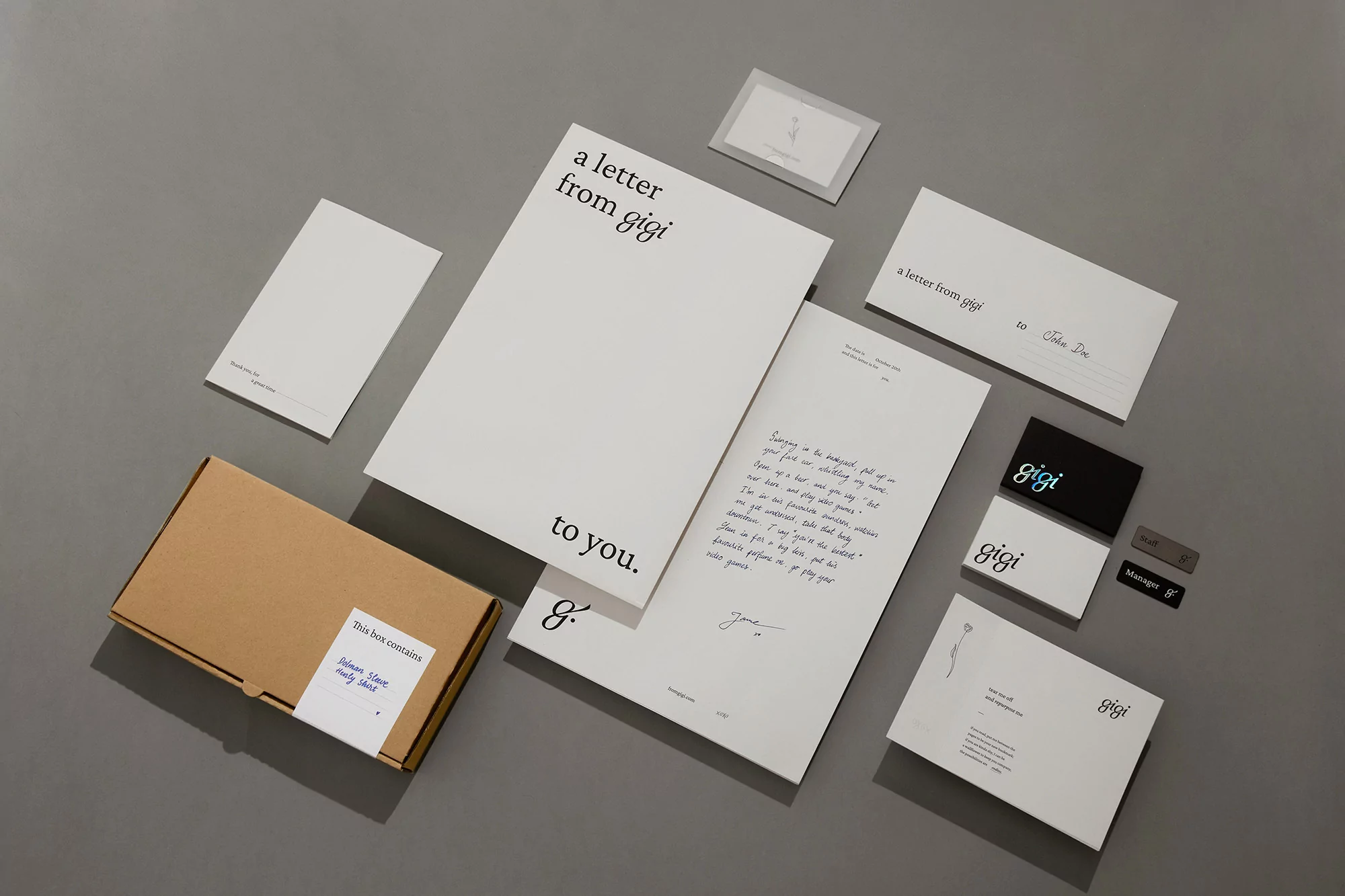 Flat lay of stationery set featuring letterhead, envelopes, cards, and a brown box on a gray surface with minimalist design elements.