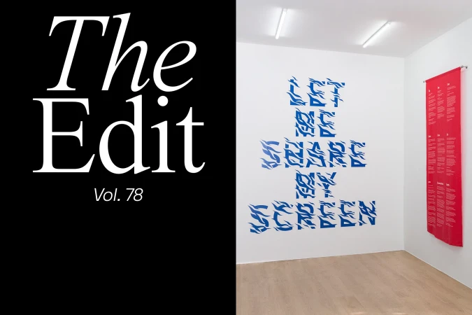 Interior of an art gallery featuring abstract blue text art on a white wall, a long red banner, and a monochrome magazine cover.