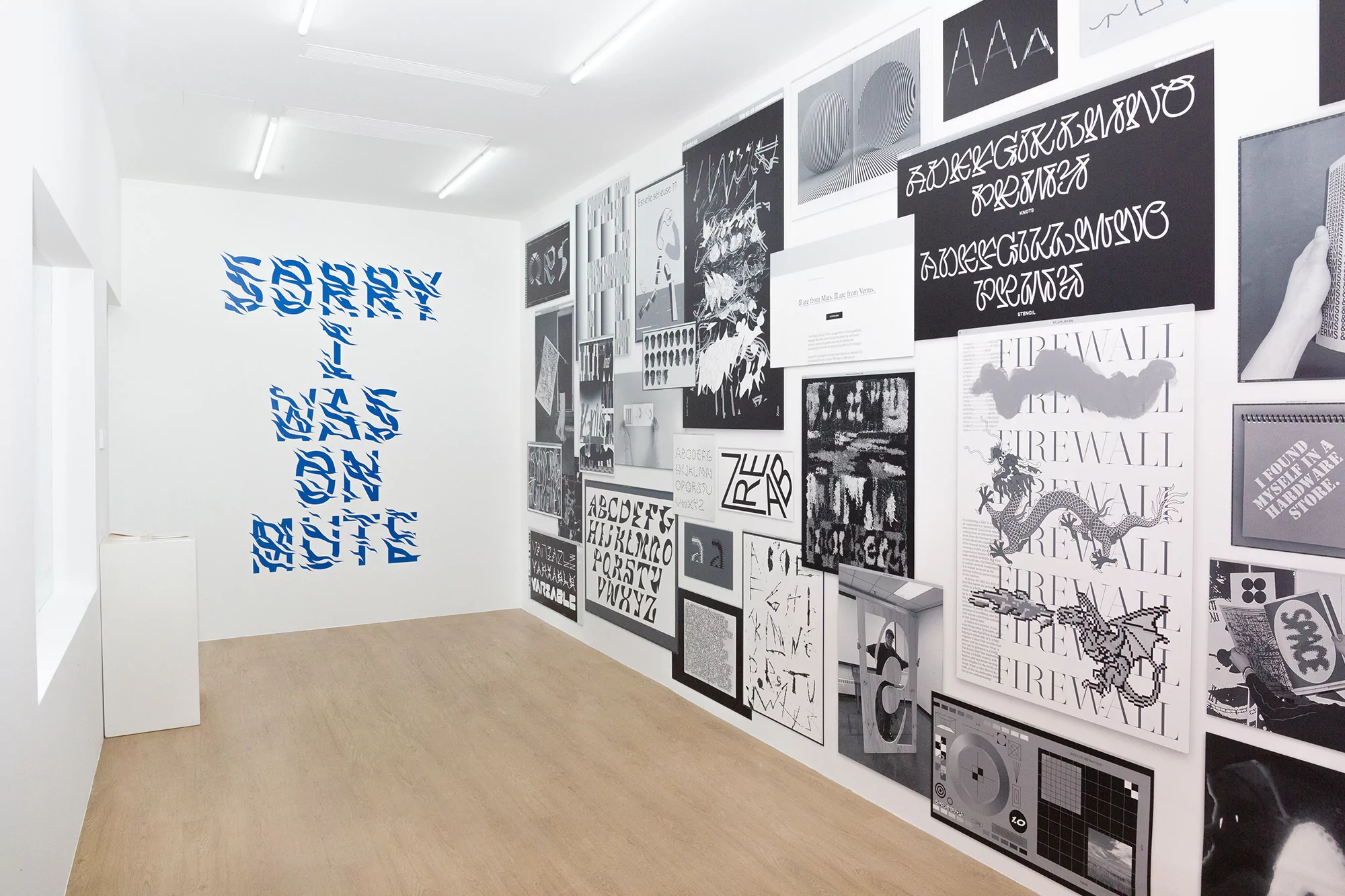 Artwork in a gallery featuring blue stylized text 'SORRY I WAS ON MUTE' and graphic posters, set in a modern, minimalist space.