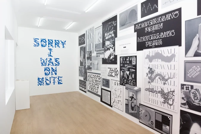 Artwork in a gallery featuring blue stylized text 'SORRY I WAS ON MUTE' and graphic posters, set in a modern, minimalist space.