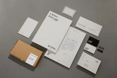 Flat lay of corporate stationery including branded letterhead envelopes business cards and a cardboard box on a grey surface.