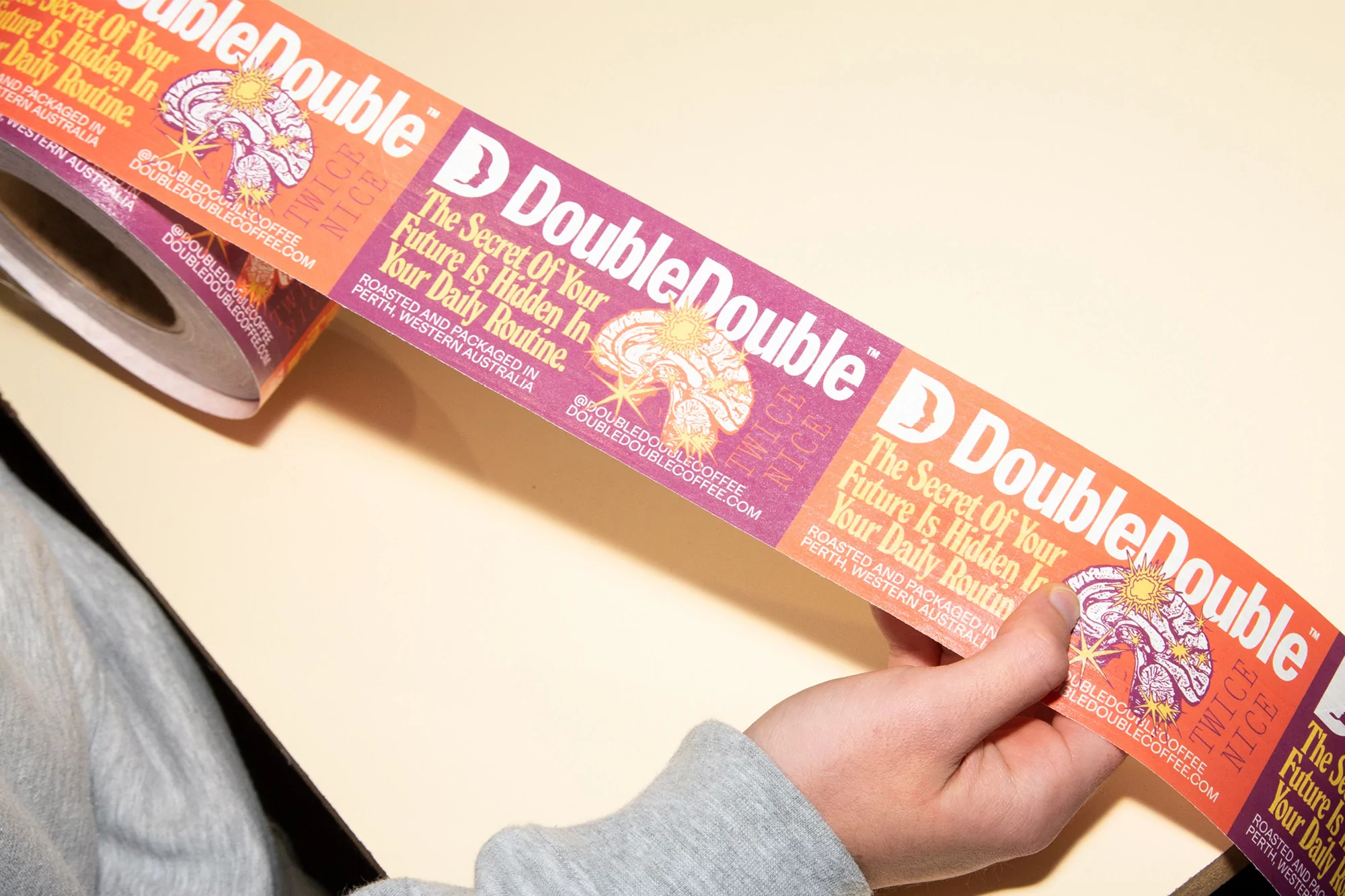 Hand holding a roll of DoubleDouble coffee stickers with the brand's logo and website visible on each label.