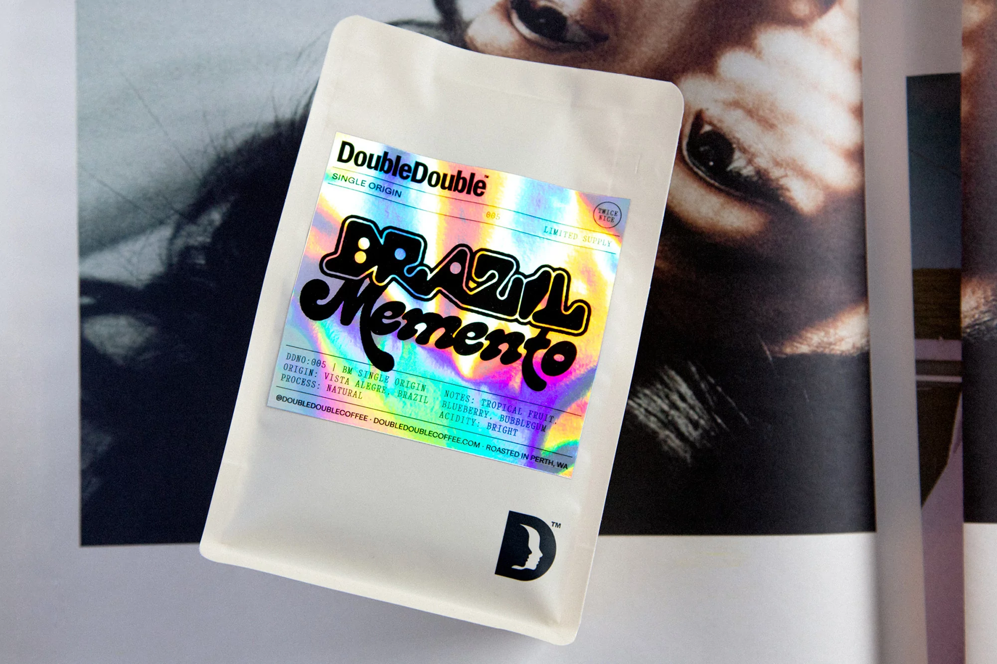 A bag of Double Double single-origin Brazil Memento coffee with a holographic label, set against a blurred magazine image.