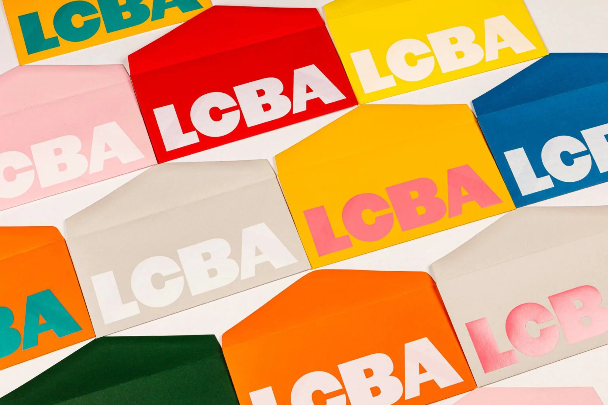 Collection of colorful envelopes with the text LCBA in white or pink, arranged on a white surface in a flat lay composition.