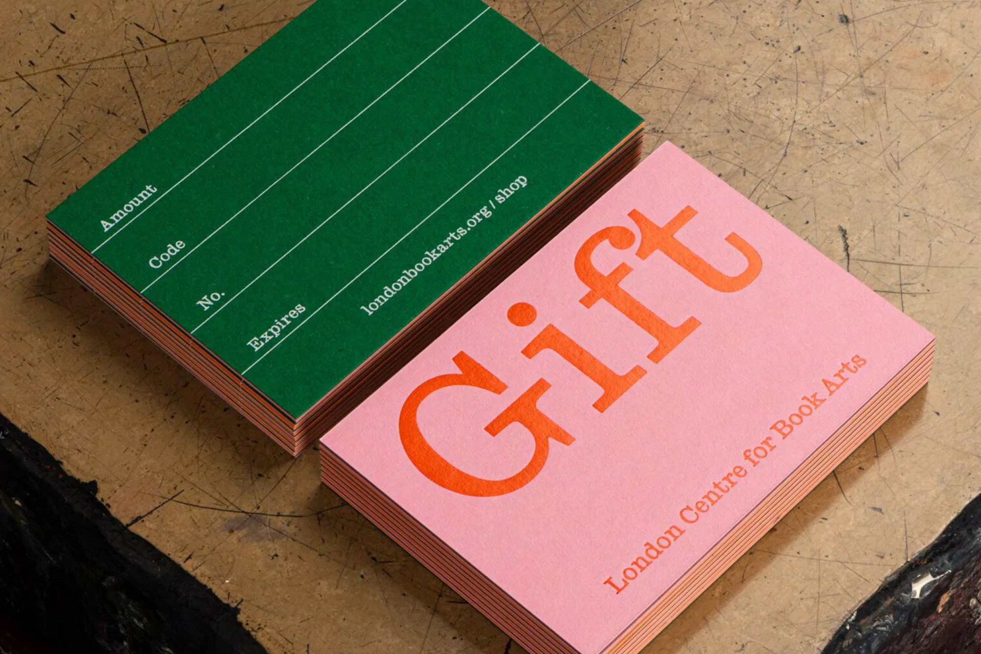 Stacks of gift cards on a table: one green with printed lines and text, the other pink with 'Gift' printed in orange.