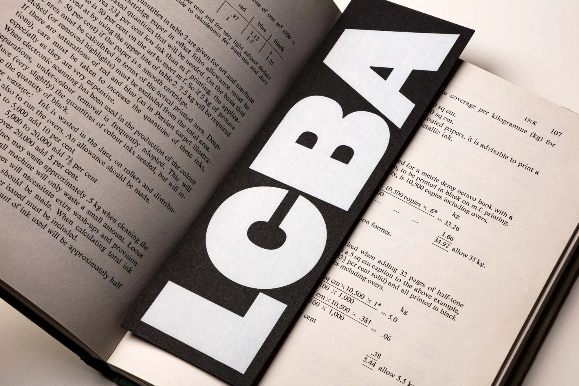 Open book with black bookmark displaying the white text 'LCBA' placed diagonally across the right page, close-up, studio lighting.