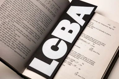Close-up of an open book displaying technical text with a bold black and white LCBA bookmark resting across the pages.