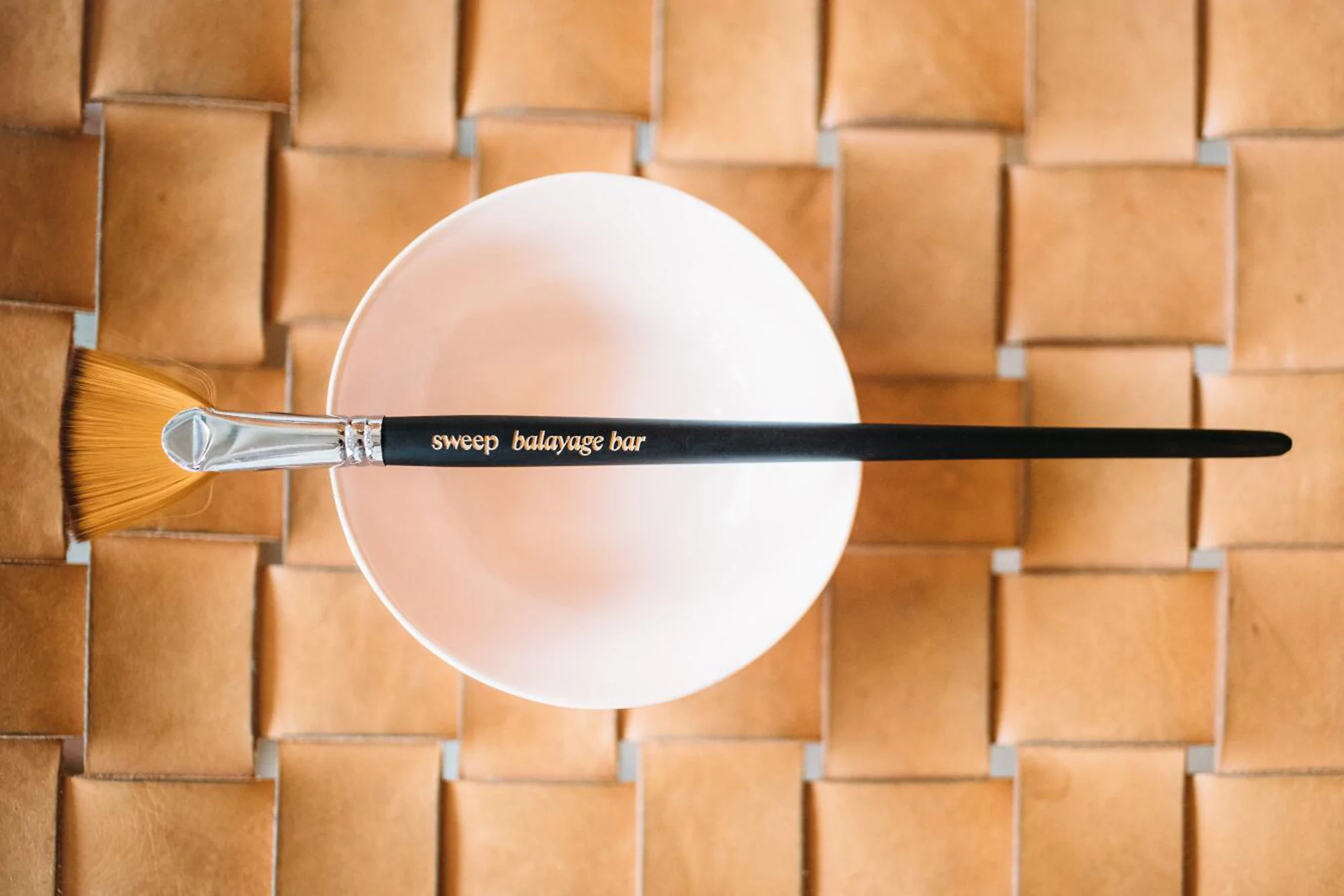 Hair coloring brush resting on a pink bowl, with a woven leather background, creating a beauty and salon-themed composition.