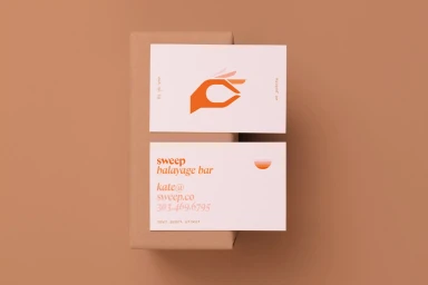 Two white business cards with orange typography resting vertically against a matching brown package.