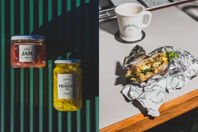 Still life of jam and pickles in glass jars, and a foil-wrapped sandwich with a mug on a table, showcasing food photography and product display.
