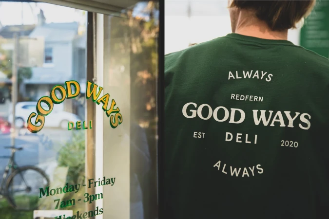 Close-up split view of Good Ways Deli branding with storefront glass lettering and person wearing green t-shirt