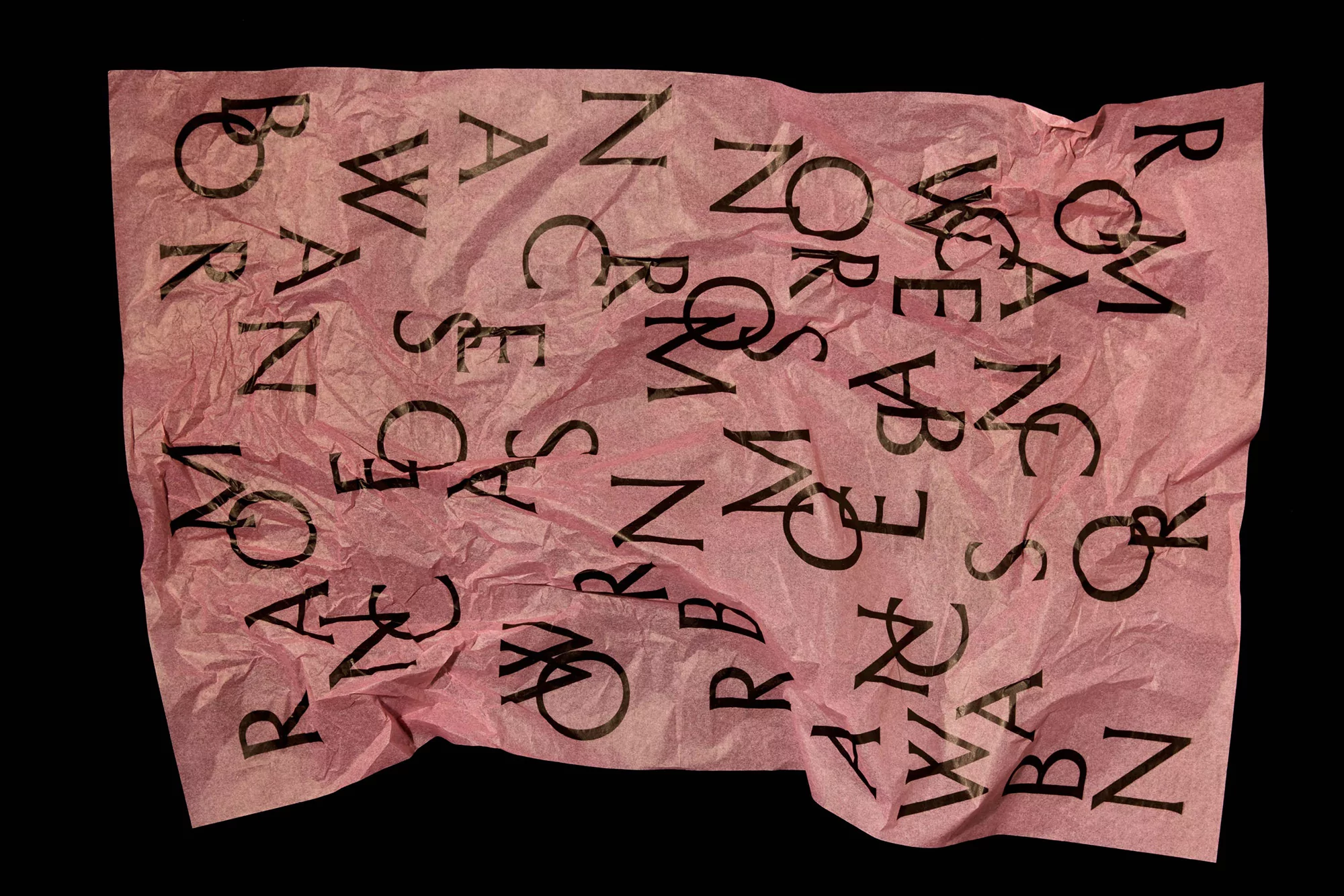 Abstract image featuring a pink crumpled sheet of paper with black lettering, set against a solid black background.