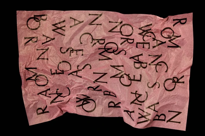Abstract image featuring a pink crumpled sheet of paper with black lettering, set against a solid black background.