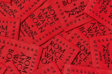 Close-up arrangement of red fabric clothing labels featuring black embroidered brand text and heart patterns.