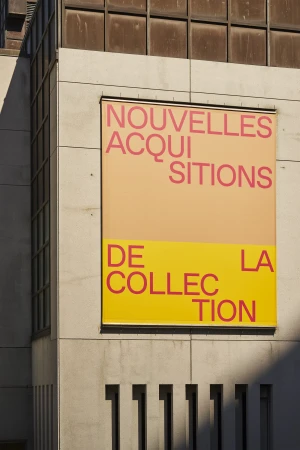 Exterior building wall with a large peach and yellow sign displaying the French text, 'Nouvelles Acquisitions De Collection La Collection'.