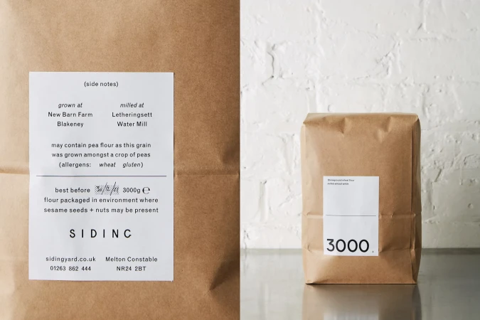 Two kraft paper bags sit against a neutral backdrop, one with a product label, the other with a detailed ingredients label.