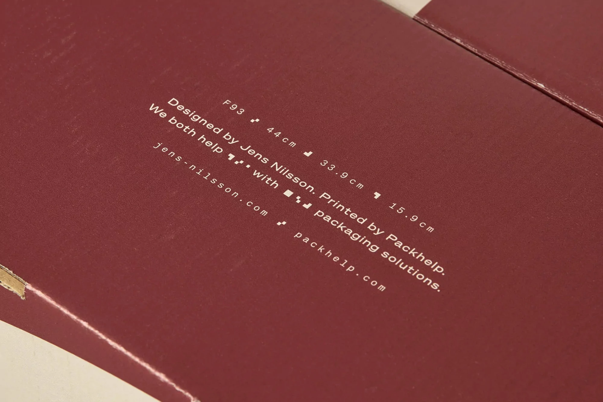 Close-up of a maroon cardboard box with white text displaying dimensions and branding details, presenting a clean and modern aesthetic.
