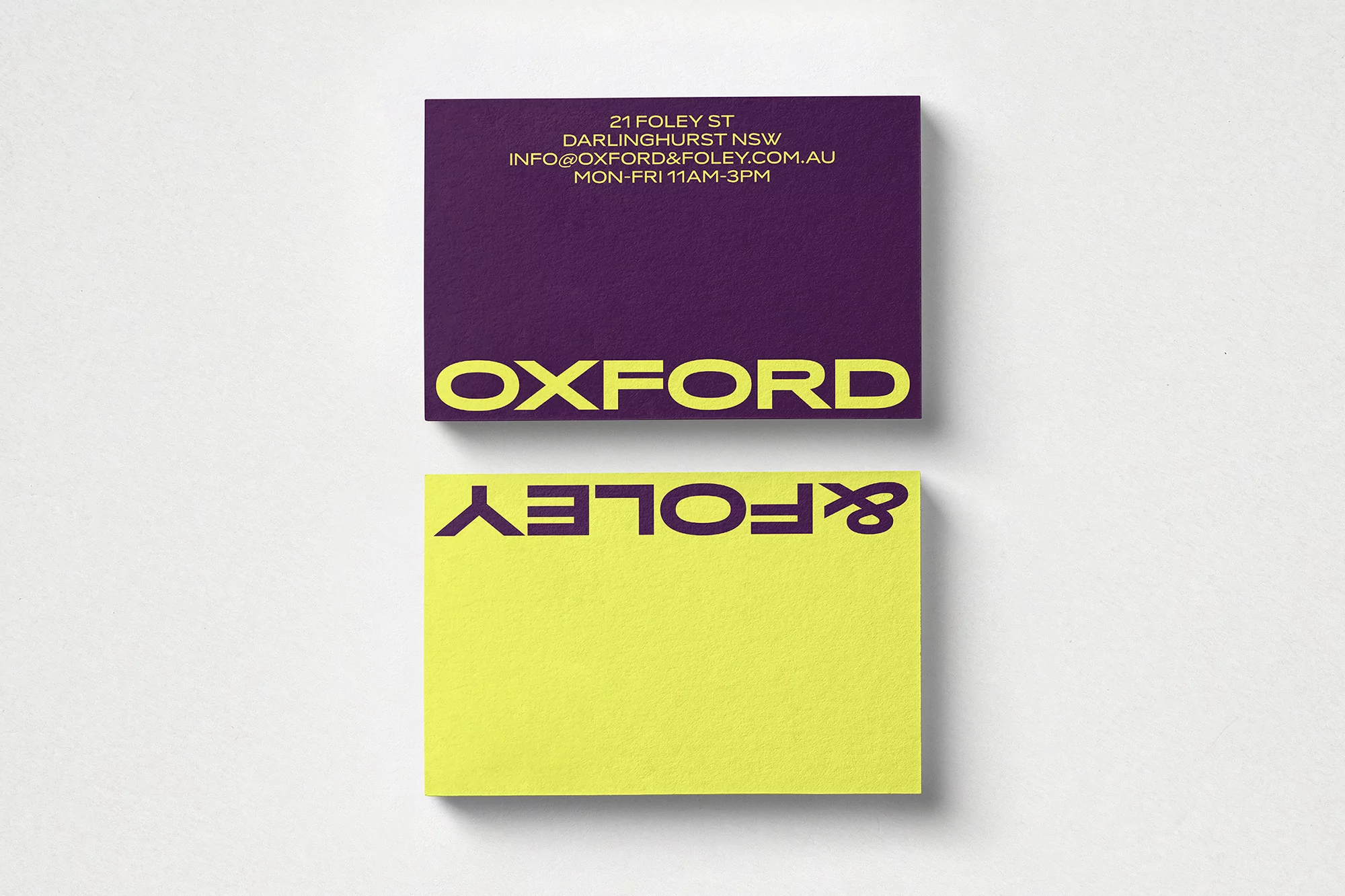 Two business cards, one violet with gold text and one chartreuse with dark violet text, are photographed against a white surface.