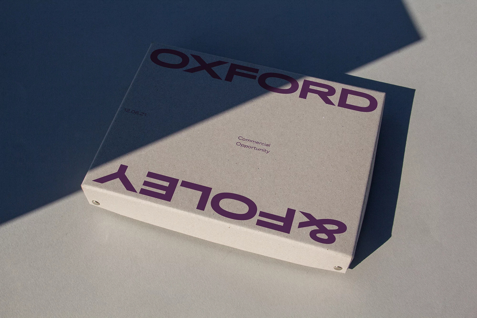 Close-up shot of a hardcover brochure with 'Oxford & Foley' text, highlighted by shadows, creating a minimalist yet professional feel.