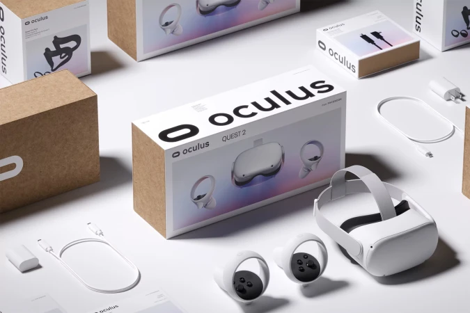 Oculus Quest 2 VR headset displayed with its box, controllers, charging cable, and power adapter on a bright white background.
