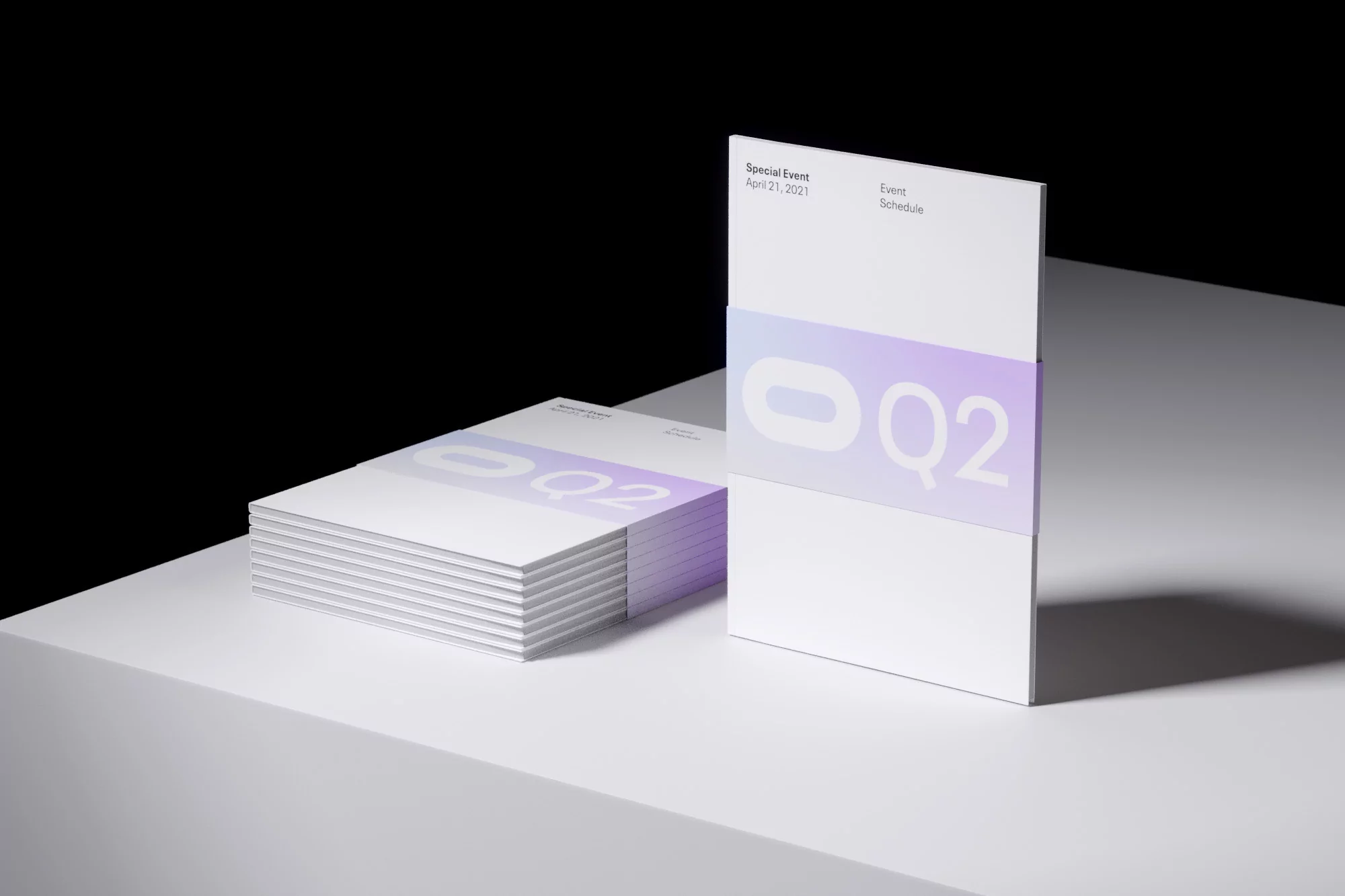 Stack of white event schedule brochures with pastel purple gradient and geometric logo; clean studio product shot with black backdrop.