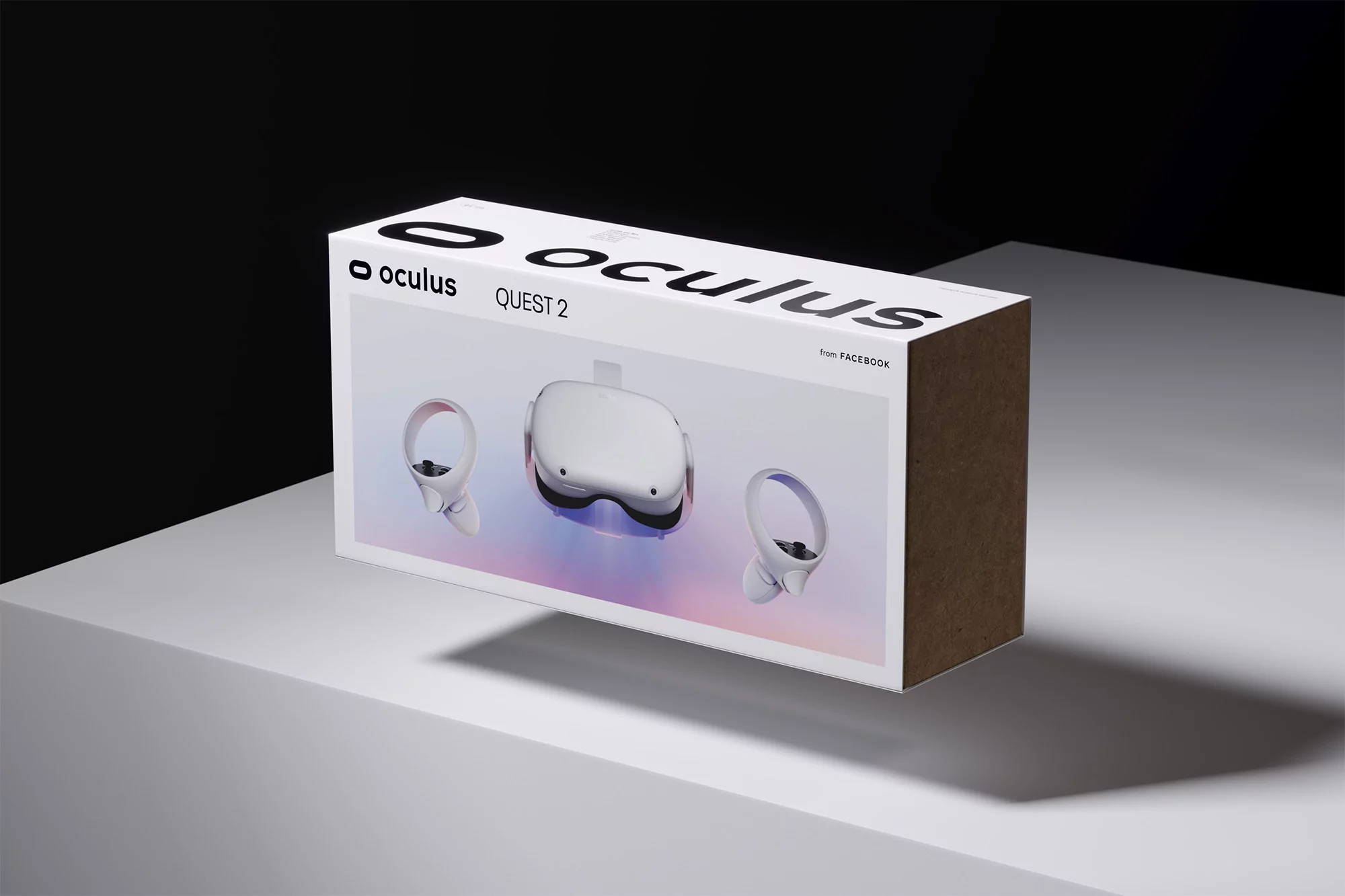 White Oculus Quest 2 box on a white surface against a dark background featuring headset and controllers on box. 