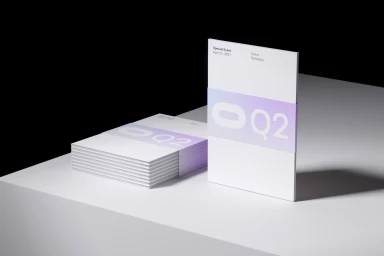 Stacks of white paper booklets with purple branded bands reading Q2 resting on a white surface.