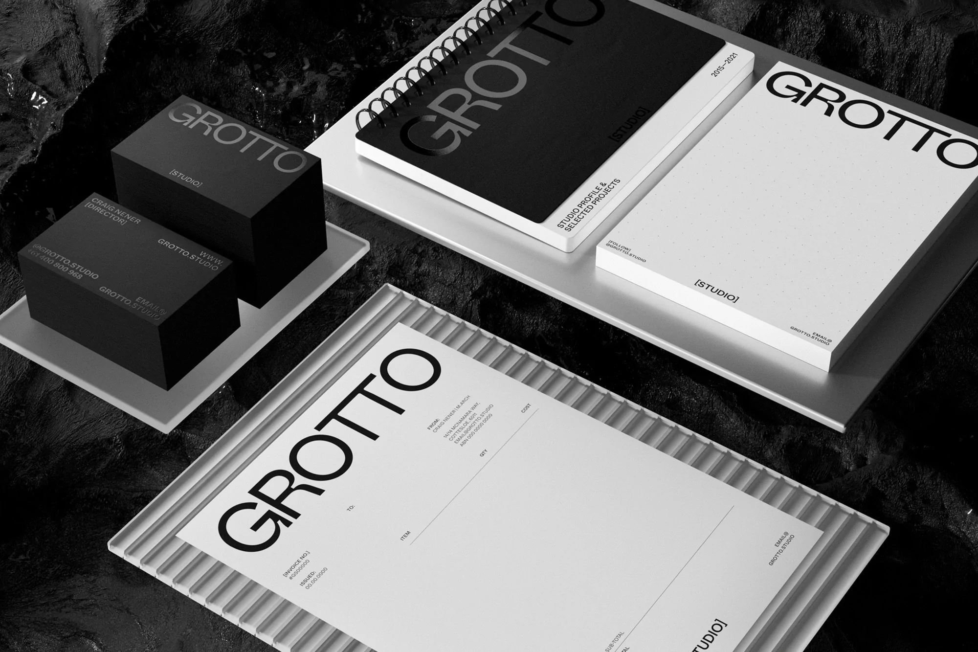 Black and white studio presentation featuring a GROTTO-branded notepad, business cards, and stationery displayed on a textured surface.
