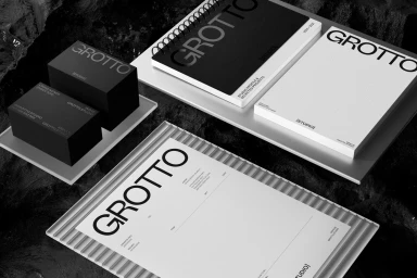 Monochrome flat lay of branded stationery items including business cards, spiral notebooks, and letterhead featuring bold typography.