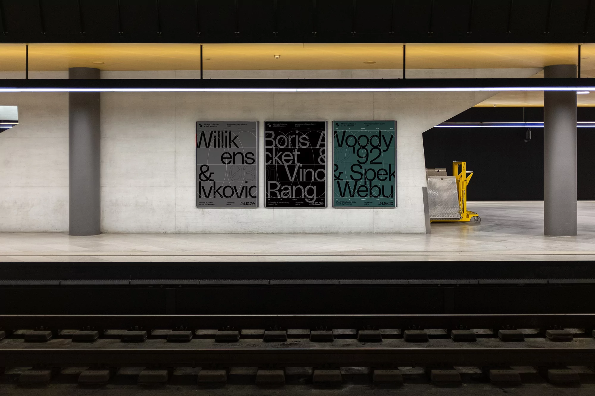 Three typographic posters hang on a concrete wall in an empty subway station, with black tracks visible at the bottom of the frame.
