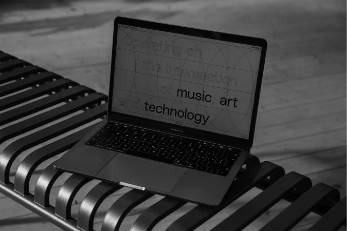 Laptop on bench displaying text about music, art, and technology, set against a blurred outdoor background in a monochrome aesthetic.