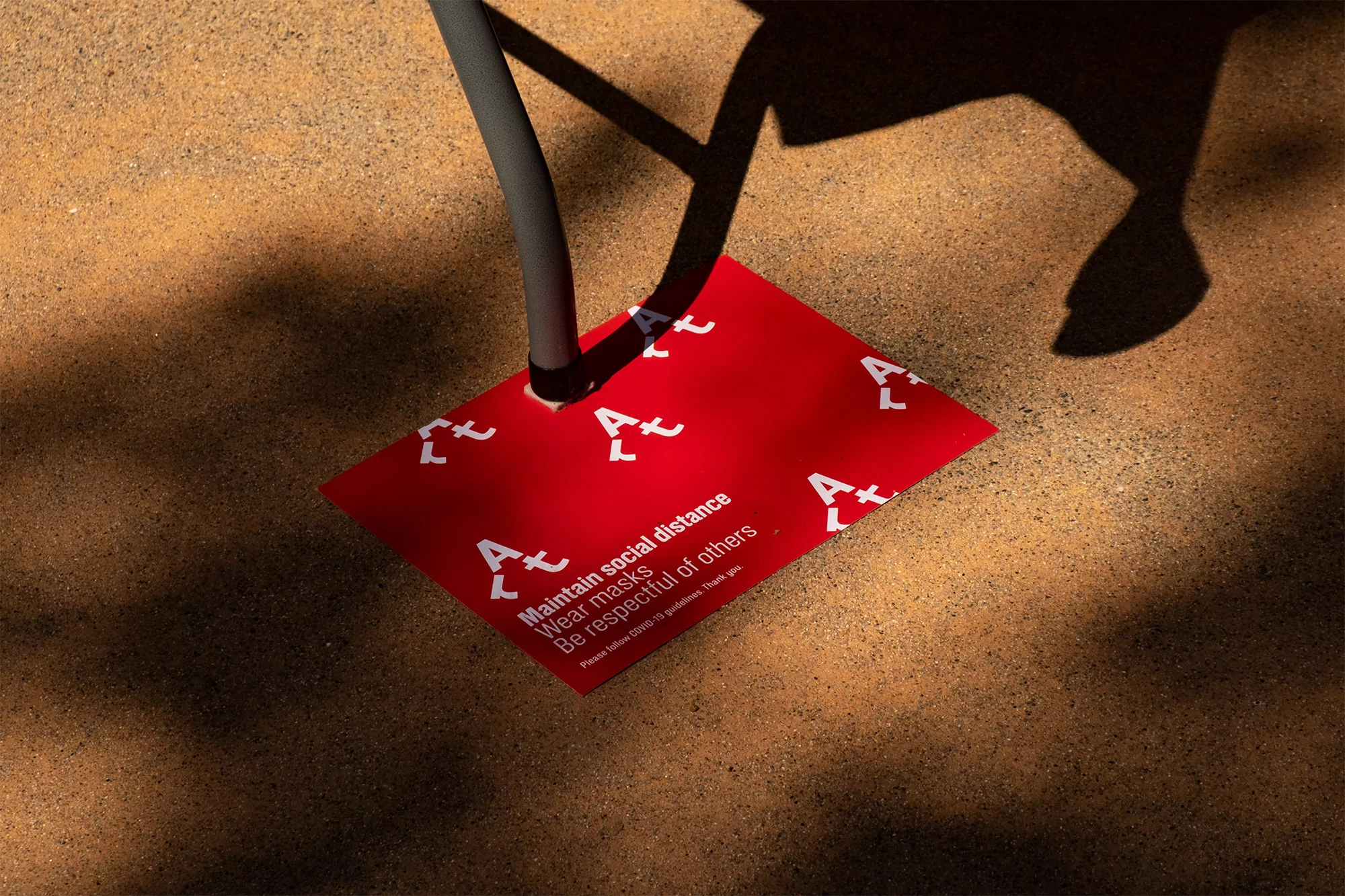 Social distancing floor sign with safety message and logo. A red square sign on the ground reminds people to maintain distance.
