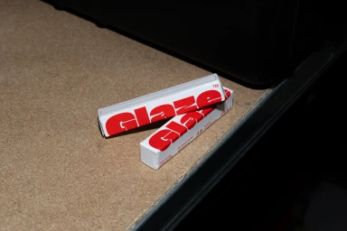 Two white paper boxes with bold red Glaze typography resting on a textured wooden workbench surface.