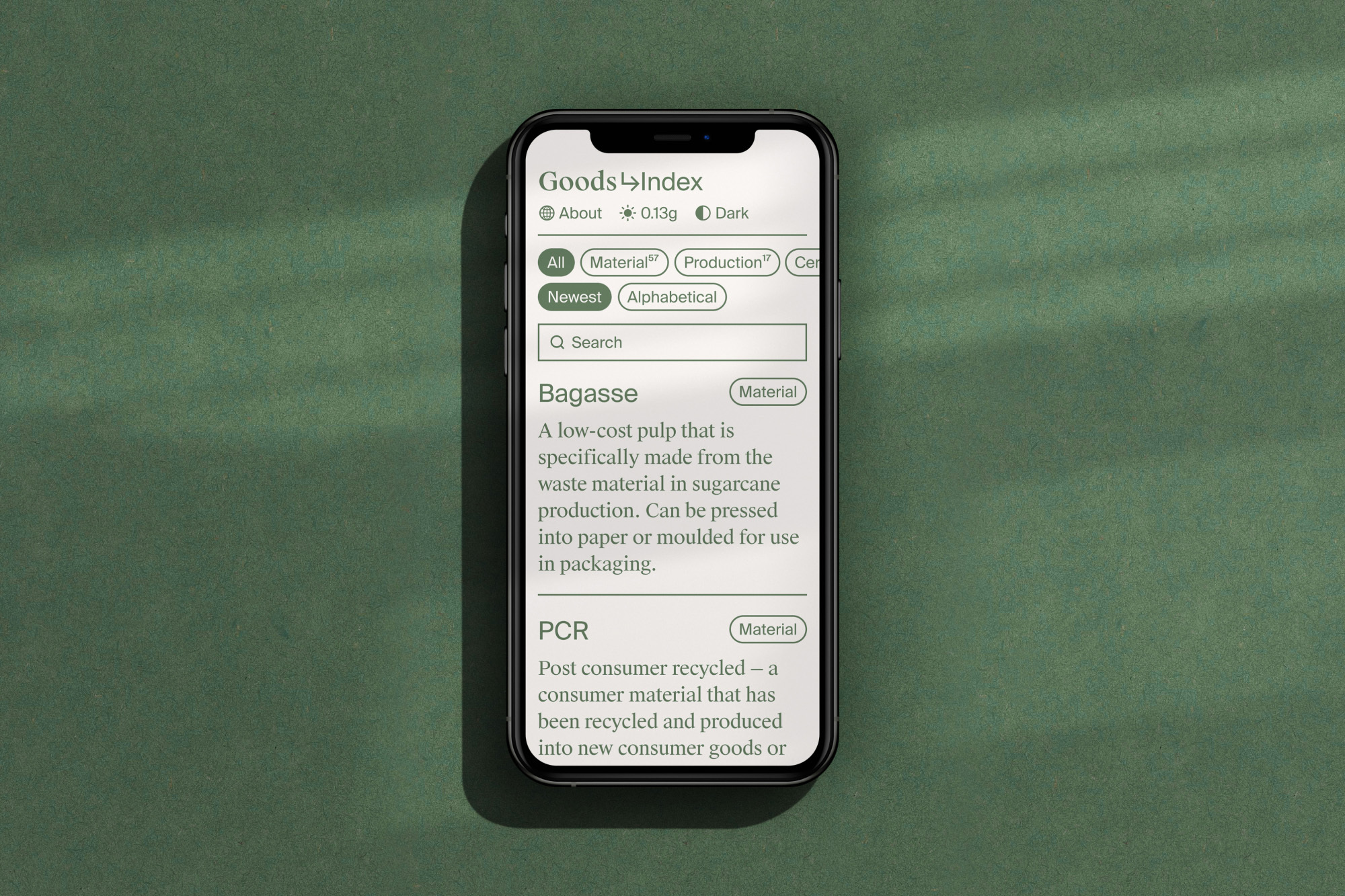 Smartphone displays a green-themed materials index app with search and information about bagasse and PCR materials on a green surface.