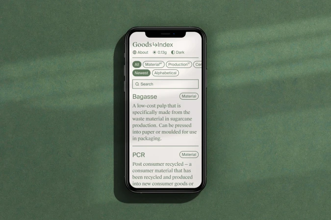 Smartphone displays a green-themed materials index app with search and information about bagasse and PCR materials on a green surface.