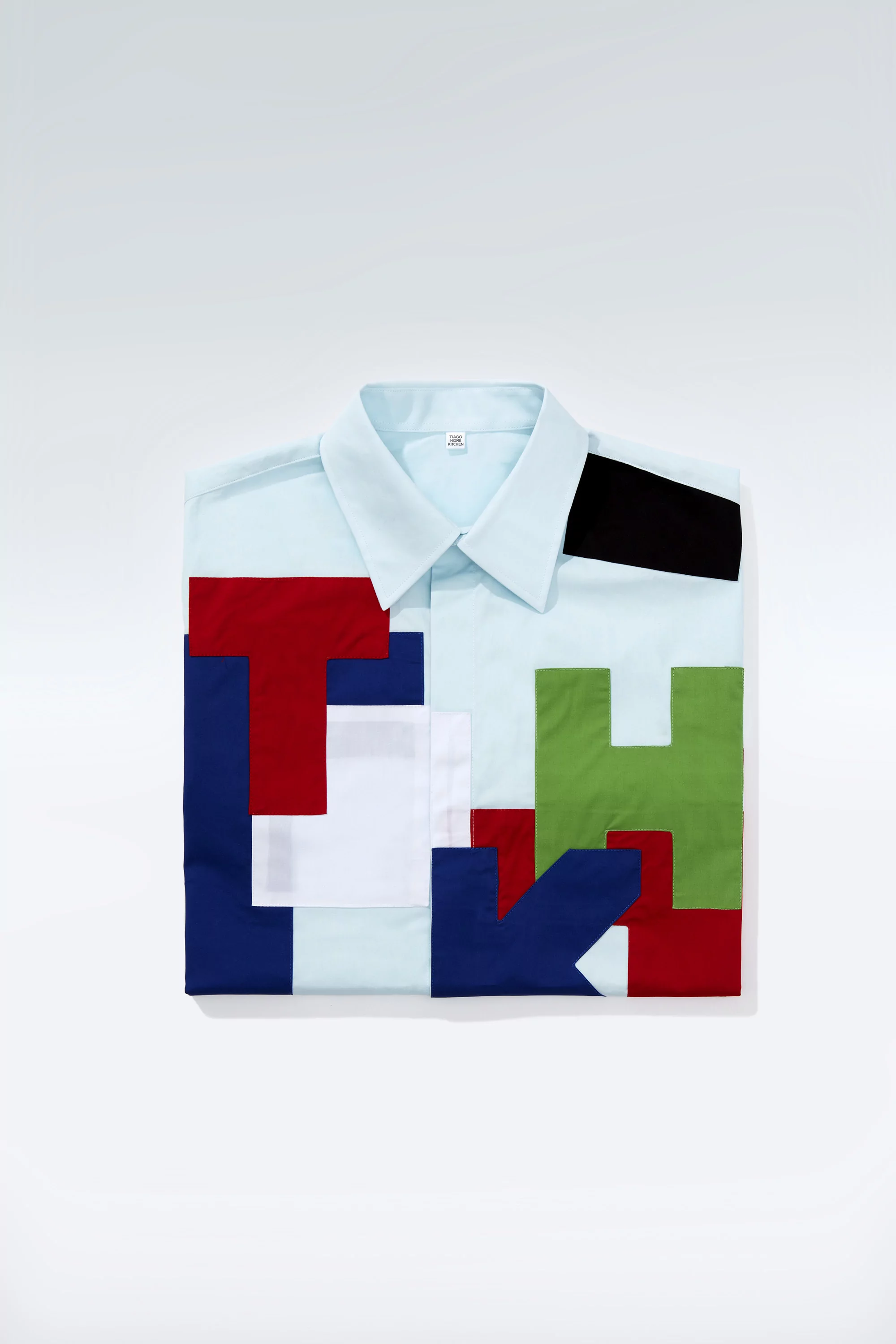 Folded light blue shirt with colourful block patchwork design on a white background, studio shot, fashion, still life.