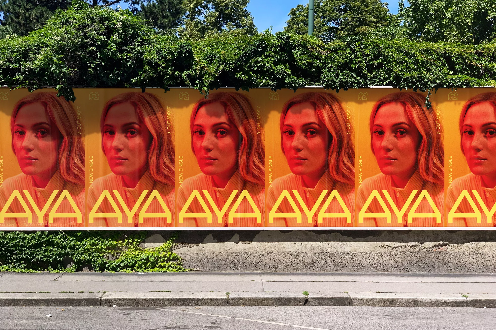 Repetitive posters of Ava Max on a concrete wall next to a sidewalk, surrounded by green trees and ivy, under a bright sky.
