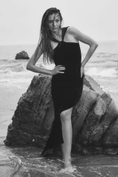 Model Miranda Kerr standing by a large coastal rock in a black dress with wet hair for Vogue Australia.