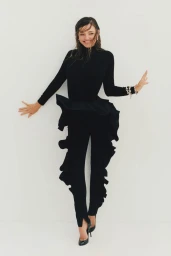 Miranda Kerr wearing a black long-sleeve top and black trousers against a plain white seamless studio background.