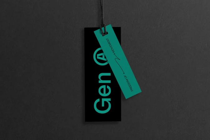 A black branded clothing tag with turquoise text Gen A and a smaller matching turquoise tag attached with string against dark textured background