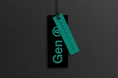 A black branded clothing tag with turquoise text Gen A and a smaller matching turquoise tag attached with string against dark textured background