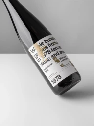 Dark glass wine bottle angled against a white surface featuring bold typographic label design by Lukas Diemling for Wild Bunch.