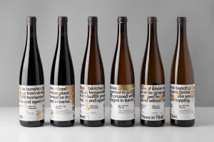 Six wine bottles with white labels featuring black typography and gold foil accents arranged in a row.