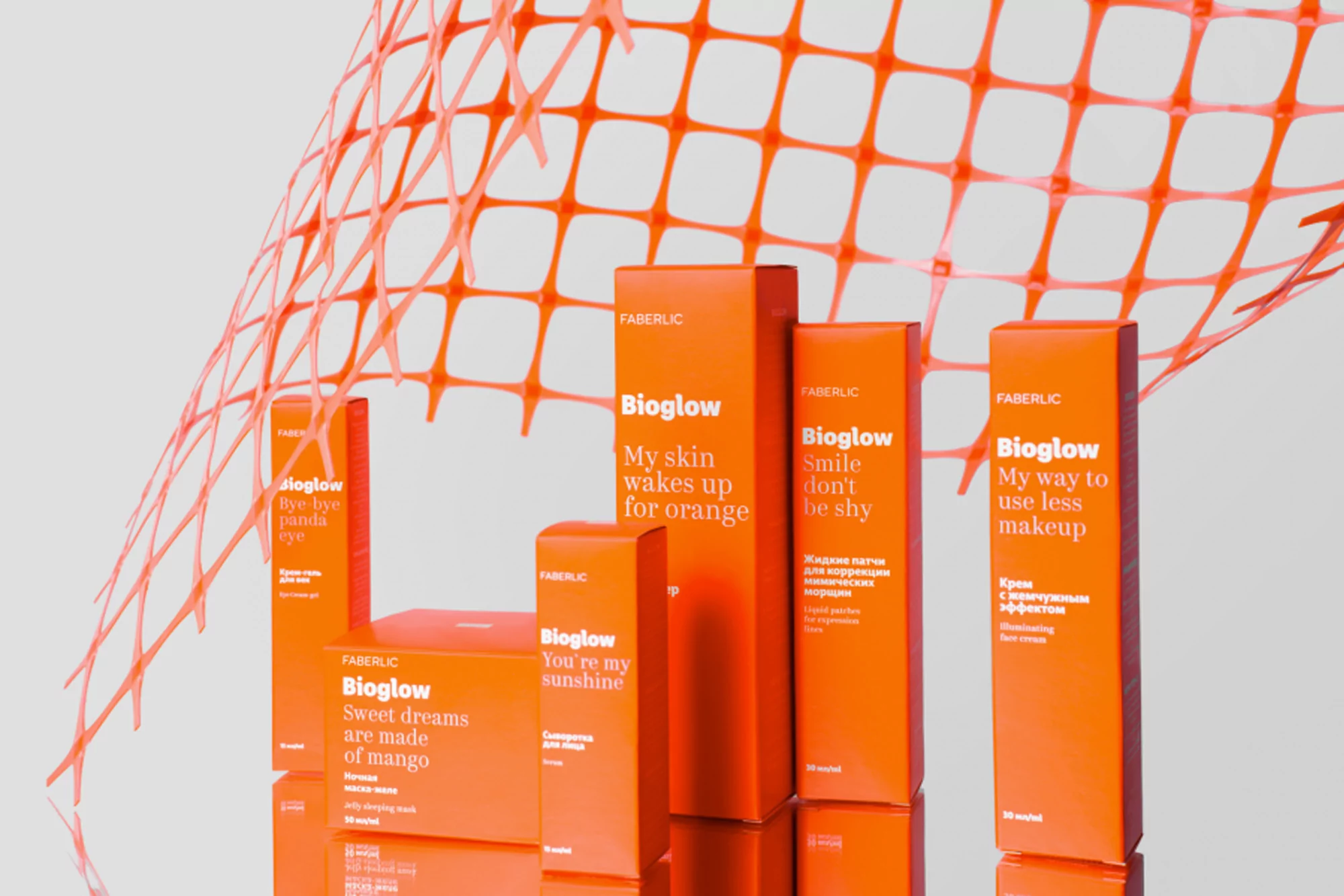 Faberlic Bioglow skin care product line in orange packaging, arranged against a light gray background with orange netting.