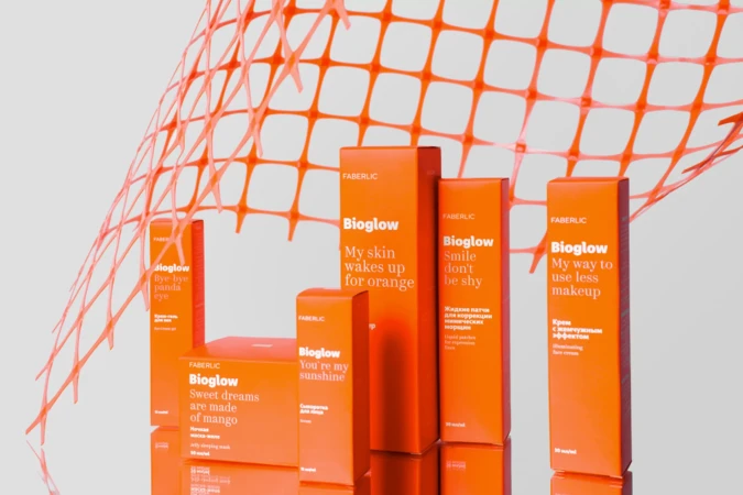 Faberlic Bioglow skin care product line in orange packaging, arranged against a light gray background with orange netting.
