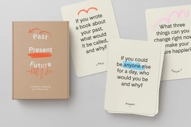 Kraft paper box and cream-colored cards with typographic questions and colored hand-drawn line accents on a neutral gray surface